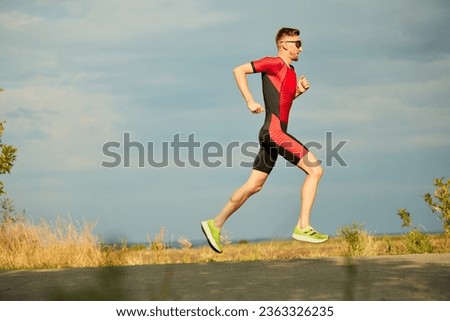 Speed and endurance. Motivated sportsman in sportswear running along the road, training outdoors. Side view. Concept of professional sport, triathlon preparation, competition, athleticism Royalty-Free Stock Photo #2363326235