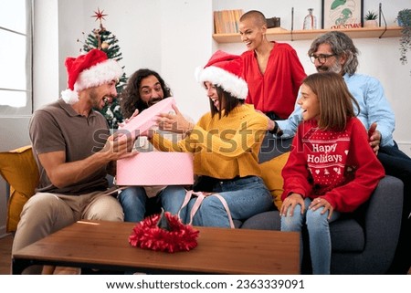 Surprised people opening Christmas presents at home. Happy and excited family gathered together on thanksgiving day for gift exchange. Positive and joyful domestic relationships in winter vacations.