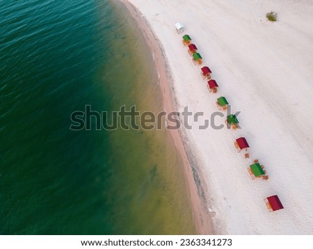 Drone shot of the beach stones tip, a sandy beach with colorful sun shades at the shore of a river with turquoise and clear water: Praia da Ponta de Pedras between Alter do Chão and Santarém in Brasil