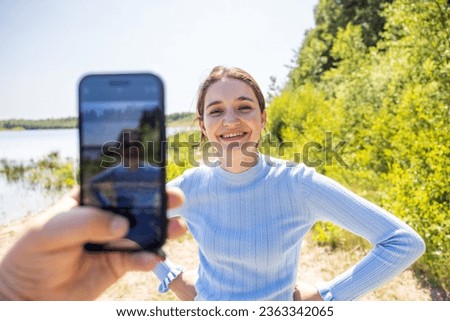 Experience the authentic connection as a male hand holds a smartphone to capture a candid moment of his attractive millennial girlfriend in the heart of summer. Their love story unfolds against the