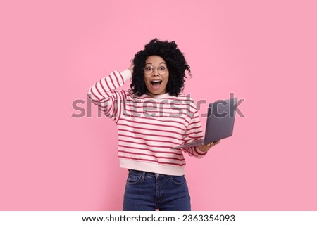 Emotional young woman with laptop on pink background