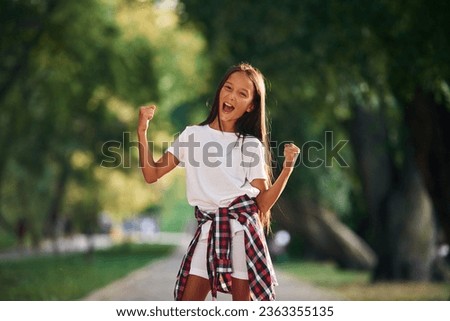 Celebrating success, happy. Young girl in casual clothes is in the public park outdoors.