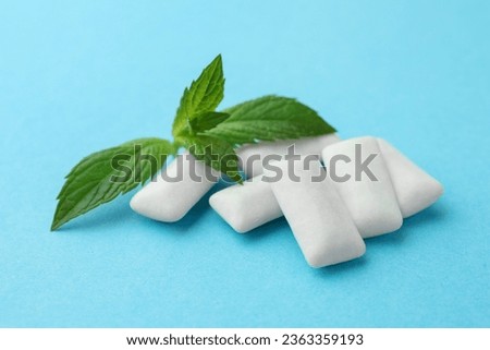 Tasty white chewing gums and mint leaves on light blue background, closeup