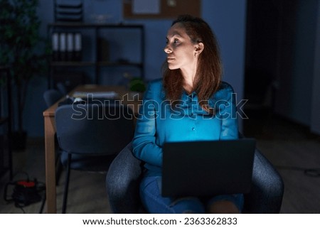 Brunette woman working at the office at night looking to side, relax profile pose with natural face with confident smile.  Royalty-Free Stock Photo #2363362833