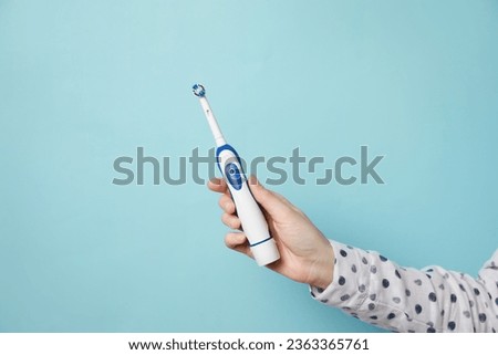 Woman holding electric toothbrush on light blue background, closeup