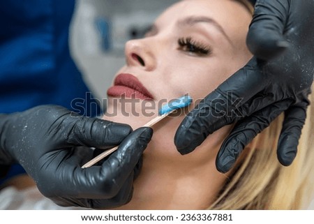 Cosmetologist doctor applies depilatory wax at lip of a young female client to remove unwanted hair. Sugar and wax Royalty-Free Stock Photo #2363367881