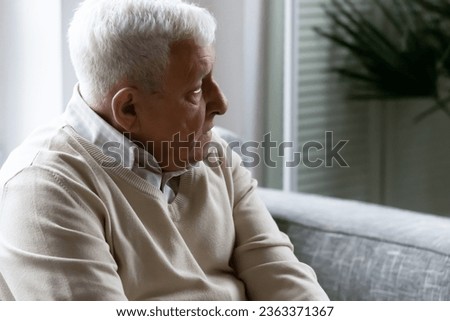 Thoughtful sad elderly 80s man sit on couch in living room look in distance thinking or pondering, feeling lonely in retirement house, pensive upset mature grandfather mourning or yearning at home Royalty-Free Stock Photo #2363371367