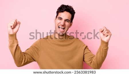 handsome hispanic man shouting triumphantly, looking like excited, happy and surprised winner, celebrating
