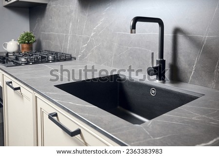 Compact undermount sink. Kitchen sink area with black square matte sink tap in contemporary style. Matte black and stoneware kitchen design. Black ceramic sink with gas hob and oven in background. Royalty-Free Stock Photo #2363383983