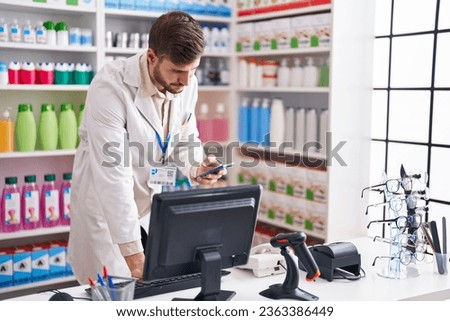 Young caucasian man pharmacist using smartphone and computer at pharmacy