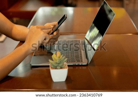 The woman is engrossed in her online shopping adventure, seamlessly transitioning between her mobile phone and laptop. With skillful taps and clicks, she explores a vast digital marketplace, close up.