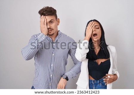 Young hispanic couple standing over white background yawning tired covering half face, eye and mouth with hand. face hurts in pain. 