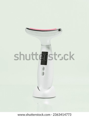 White Face and Neck Beauty Device Massager with Red Light Therapy on pastel green background 