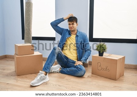 Young hispanic man sitting on the floor at new home confuse and wonder about question. uncertain with doubt, thinking with hand on head. pensive concept. 