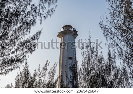 Pandansari beach lighthouse behind green trees with bright blue sky as a background