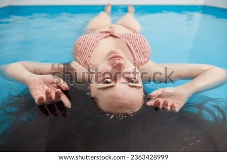 Woman looks at the camera lying in the water of a saltwater pool. Spa treatments.