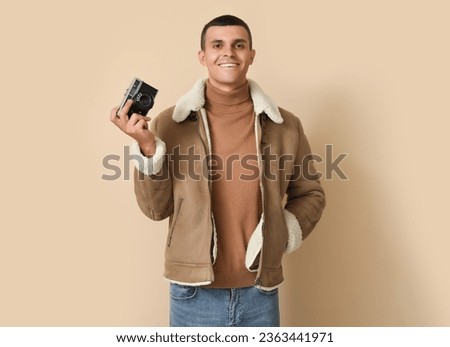 Young man in sheepskin jacket with photo camera on beige background