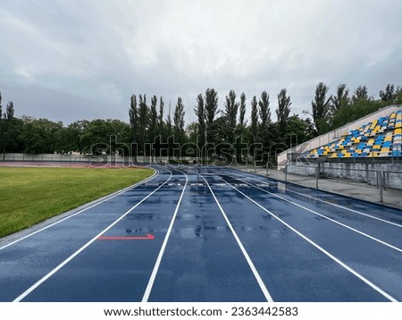 Picture of a blue running track and a green soccer field on a rainy day with cloudy sky. Rainy day and track.  