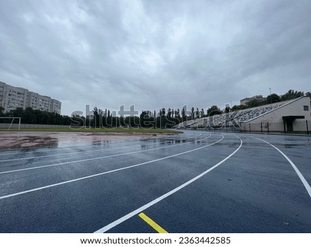 Picture of a blue running track and a green soccer field on a rainy day with cloudy sky. Rainy day and track.  