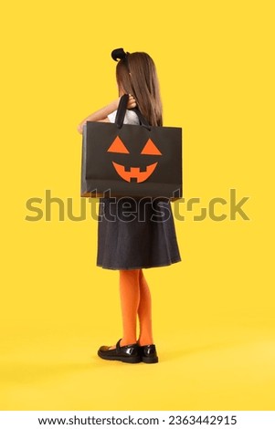 Little girl dressed for Halloween with gift bag on yellow background