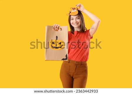 Young woman with Halloween gift bag on yellow background