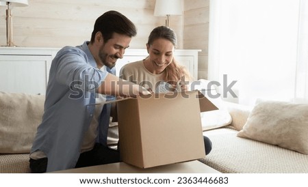 Happy young couple unpacking awaited parcel at home together, curious man and woman looking into open cardboard box, satisfied customers received online store order, good delivery service Royalty-Free Stock Photo #2363446683