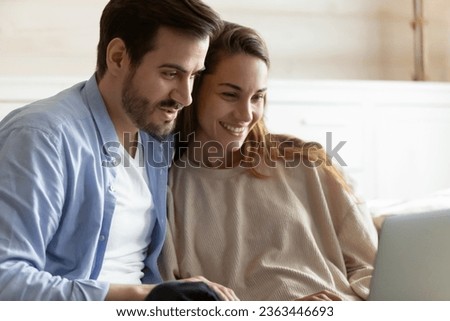 Smiling woman and man using laptop close up, hugging and looking at screen together, loving young couple shopping online, using internet banking services, watching movie, enjoying leisure time