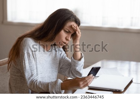 Angry young woman looking at phone screen, reading bad news in email or social network message, unpaid debt or spam, annoyed girl having problem with broken or discharged smartphone Royalty-Free Stock Photo #2363446745