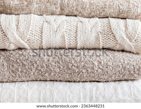 Pile of cozy light knitted clothes and blankets for cold weather. Comfort organic sweaters and plaids. Hygge style idea