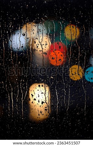 Rainy wet window at night with water drops and colorful city lights