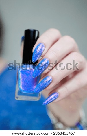 Woman's beautiful hand with long nails and light blue and pink manicure with bottles of nail polish