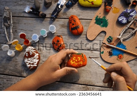 Diy concept. A detailed picture of a child's hands drawing on stones Halloween characters. Art project for children. Party decor.