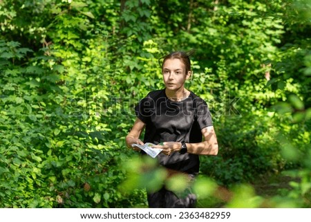 Young girl in forest reading map and searching for a control point. Sports orienteering competition. Athlete teenager girl moving to the control point Royalty-Free Stock Photo #2363482959