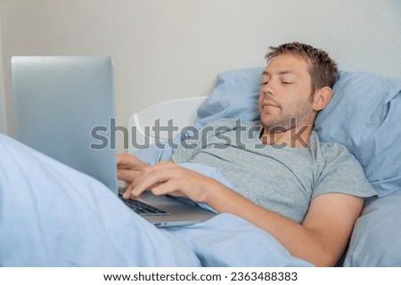 Male freelancer working with laptop in bed in the morning. Man designer on remote work from home. Wireless technology 