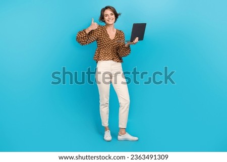 Full size portrait of cheerful nice girl hold wireless netbook hand finger demonstrate thumb up isolated on blue color background