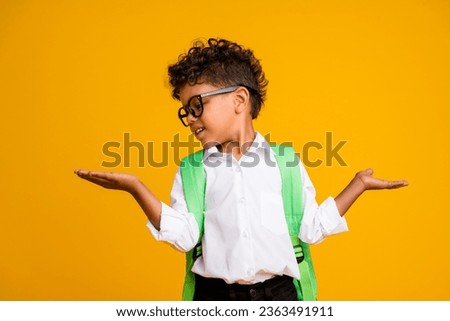 Portrait of cute small schoolkid look hands hold show empty space scales proposition isolated on yellow color background