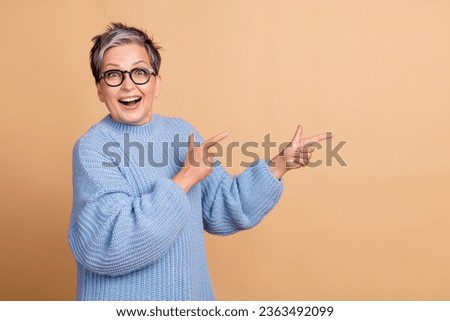 Photo portrait of attractive senior woman point excited empty space wear trendy blue knitwear clothes isolated on beige color background