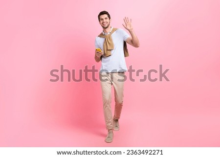 Full size body photo of friendly young guy palm hello greetings all fans holding smartphone chatting isolated on pink color background