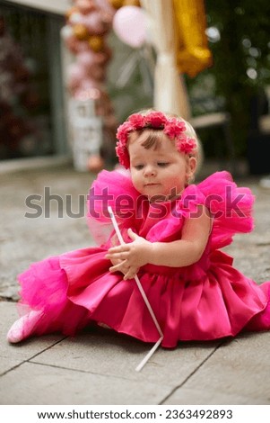 birthday of a little girl in an elegant raspberry-colored dress with flowers on her head