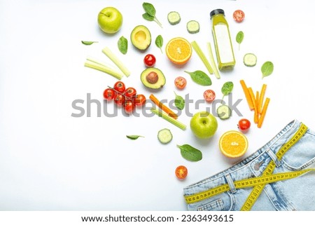 Fresh fruit, vegetables, smoothie falling into jeans and yellow measuring tape instead of belt on white background. Concept of weight loss, detox, diet, healthy clean nutrition, space for text Royalty-Free Stock Photo #2363493615