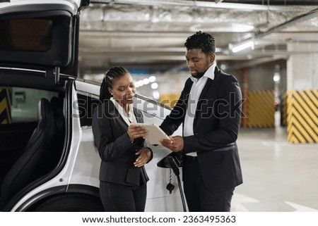 African american male in business suit putting electronic signature on document via tablet during e-car fill-up in garage. Fellow employees saving time and money while using modern technologies.