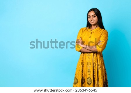 Beautiful Middle Eastern Young Lady In Traditional Yellow Dress Posing And Advertising Great Fashion And Beauty Offer, Standing Near Free Space Over Blue Studio Background, Smiling To Camera Royalty-Free Stock Photo #2363496545