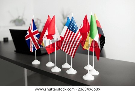 Many Different Countries Flags And Laptop Computer Standing On Office Table During International Conference Meeting. No People, Objects. Global Online Business And Education Abroad Concept