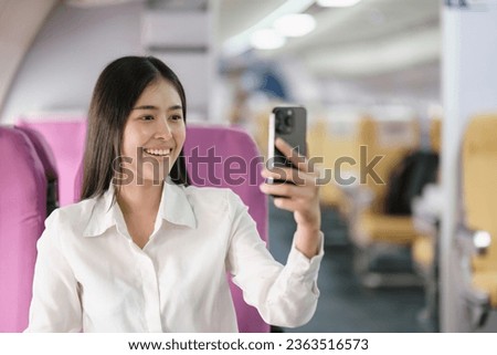 Smiling tourist woman taking a selfie on her mobile phone waiting on the plane. Passengers traveling abroad during the weekend air flight concept