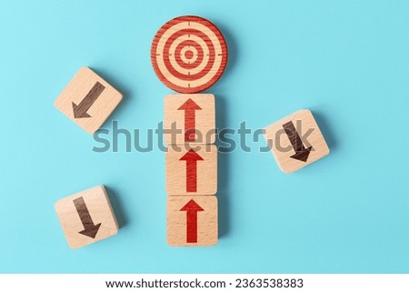 Wooden blocks with target and upward and downward arrows. Concept of right and systematic way to achieve the goal