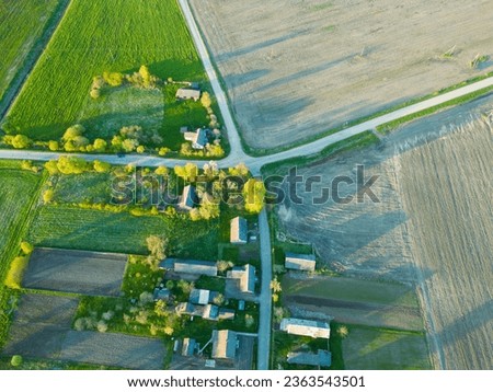 Aerial view over a small village near a dirt road. Large multi-colored fields planted with various agricultural crops. Wheat field from a bird's-eye view. Royalty-Free Stock Photo #2363543501