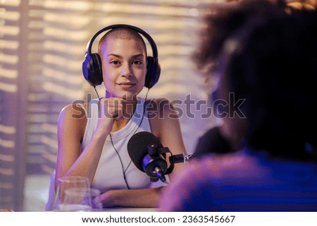 Portrait of a host sitting with a colleague in a small home recording studio and wearing headphones while smiling at the camera. Podcasters are ready to go live on stream on the internet.