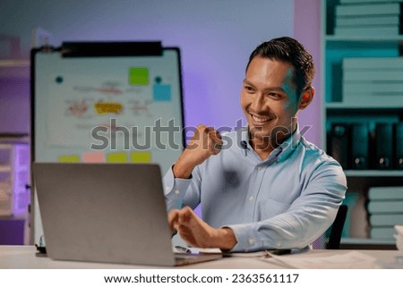 Asian man showing happy expression in the office, company employee working overtime, working late at night, working overtime of a busy and hardworking company employee. Overtime concept. Royalty-Free Stock Photo #2363561117