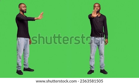 Negative person raising hand doing stop sign on camera, expressing rejection and denial. Young male adult being displeased and showing refusal gesture, no symbol on green screen.