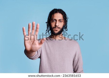Arab man making stop gesture with hand and looking at camera with serious face expression portrait. Confident young person showing warning and rejection sign with arm concept